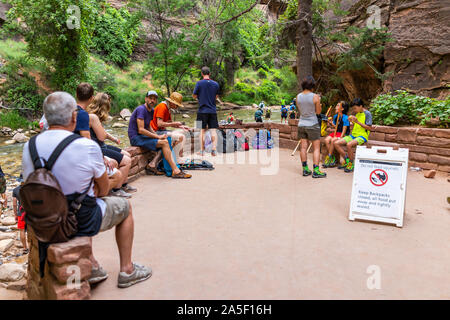 Springdale, Stati Uniti d'America - 6 Agosto 2019: Parco Nazionale Zion Riverside si restringe a piedi il sentiero in Utah con gente seduta in appoggio vicino al fiume con segno Foto Stock