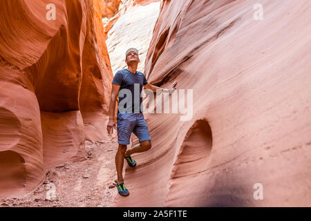 L'uomo escursionista cercando di toccare la parete di onda rossa formazioni di forma ad asola Antelope Canyon in Arizona sul sentiero sentiero dal lago Powell Foto Stock