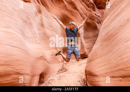 Uomo felice escursionista jumping fino a braccia alzate da onda rossa formazioni di forma ad asola Antelope Canyon in Arizona sul sentiero sentiero dal lago Powell Foto Stock