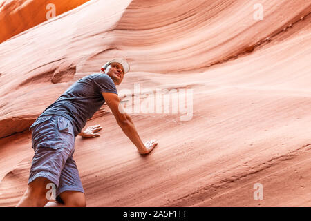 L'uomo escursionista salendo di toccare la parete di onda rossa formazioni di forma vista in slot Antelope Canyon in Arizona sul sentiero sentiero dal lago Powell Foto Stock
