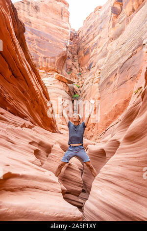 Colorate formazioni di arenaria e uomo salendo in piedi sulla cima della roccia a braccia alzate cercando fino a slot Antelope Canyon in Arizona sul sentiero dal lago di Po Foto Stock