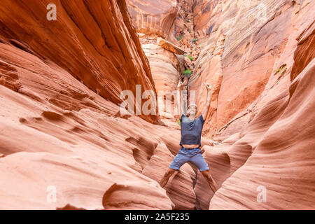 Colorate formazioni di arenaria e uomo in piedi sulla sommità della roccia a braccia alzate cercando fino a slot Antelope Canyon in Arizona sul sentiero dal lago Powell Foto Stock