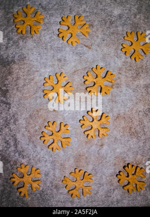 Gingerbread cookie sono tagliati in forma di un fiocco di neve fatto da impasto crudo su pergamena carta da forno su uno sfondo scuro. Vista da sopra. salvare spazio Foto Stock