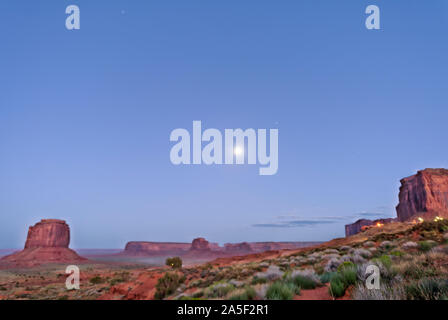 Butte formazioni di roccia rossa colore nella Monument Valley canyon nel crepuscolo di notte oscura in Arizona con vetture su polvere di strada sterrata e la luna nel cielo Foto Stock