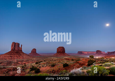 Mesa famoso Butte formazioni di roccia rossa colore nella Monument Valley canyon nel crepuscolo di notte oscura in Arizona con vetture su strada sterrata e Luna in s Foto Stock