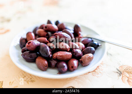 Macro Closeup di rosso porpora marinata di olive kalamata sulla piastra bianca in Italia o in Grecia per servire come antipasto sulla tabella di impostazione di partito Foto Stock