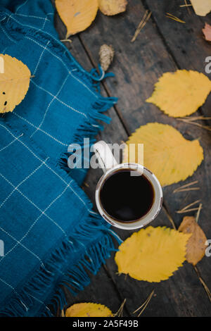 Su un vecchio tavolo di legno in autunno park è una tazza di tè e caffè. Un caldo blu plaid sciarpa è diffusa con foglie di giallo e pigne. Vista superiore Foto Stock