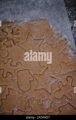 Tagliare gingerbread cookie nella forma di un albero di Natale, stella piccolo uomo, cuori da impasto crudo su pergamena carta da forno su uno sfondo scuro Foto Stock