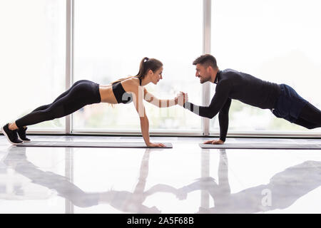 Due persone che amano la palestra fitness sono in piedi su una mano nella posizione dell'asse e trattenere reciprocamente con un'altra mano con un sorriso. È bello e adorabile Foto Stock