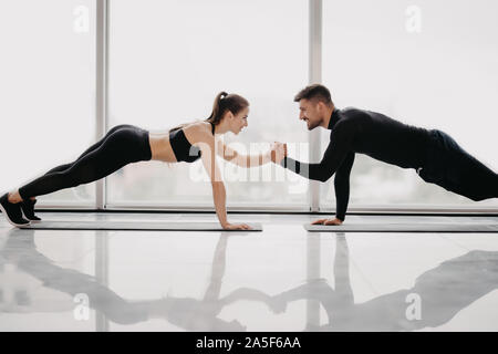 Giovane coppia sportiva lavorando insieme in una palestra . Facendo esercizi tavoloni tenendo gli uni con gli altri per una mano. Foto Stock