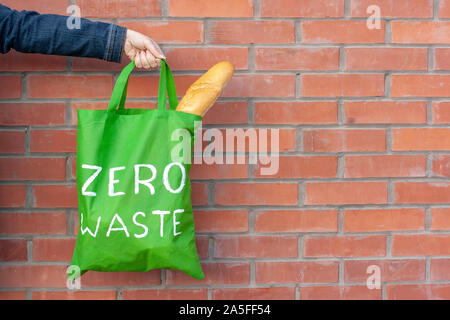 Eco sacchetto con la scritta rifiuti zero in mano su uno sfondo di un muro di mattoni con una copia dello spazio. Pane francese bastoni fuori del sacchetto. Foto Stock