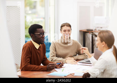 Multi-etnico gruppo di studenti sorridente felicemente mentre è seduto alla scrivania in college, concentrarsi sulla bella ragazza in centro, spazio di copia Foto Stock