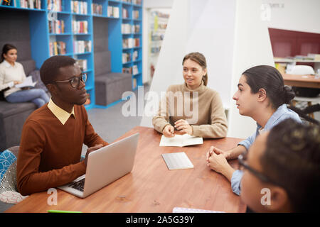 Elevato angolo di visione a multi-etnico gruppo di studenti che lavorano sul progetto team in biblioteca, concentrarsi su sorridente afro-americano di uomo porta incontro, spazio di copia Foto Stock