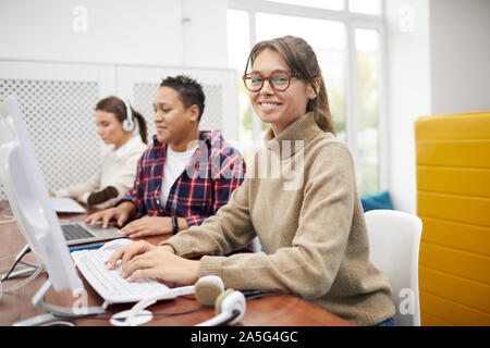 Ritratto di giovane e bella donna sorridente in telecamera mentre si utilizza il computer in un college biblioteca, spazio di copia Foto Stock