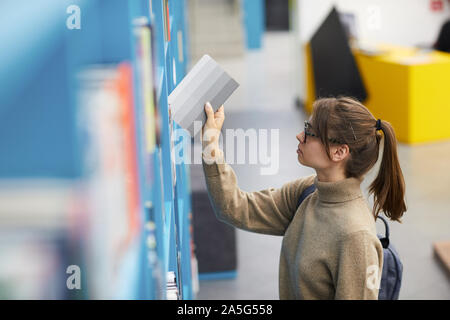 Angolo alto ritratto femminile di studente di college la scelta di libri in piedi da ripiani in biblioteca, spazio di copia Foto Stock