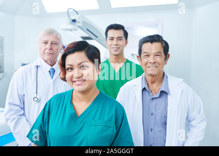 Allegro chirurgo, medici e infermiere in piedi nella stanza di ospedale e sorridente in telecamera Foto Stock