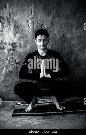 Ragazzo adolescente nero che indossano costumi colorati e fare yoga il coloratissimo tappeto tradizionale e facendo del famoso Garland porre o Malasana. Colpo verticale. Foto Stock