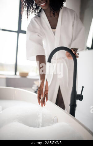 Donna cerca la temperatura dell'acqua durante la preparazione della vasca da bagno Foto Stock