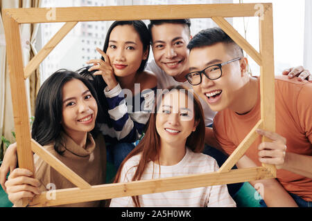 Gruppo di felice friendly giovani asiatici persone azienda legno cornice fotografica e che pongono in telecamera Foto Stock