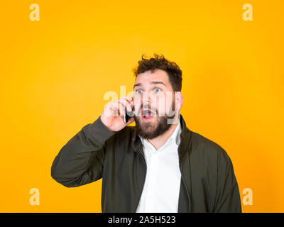 Raffreddare l'uomo con lo smartphone, nero di barba e capelli neri è in posa di fronte di sfondo arancione e facendo diverse espressioni Foto Stock