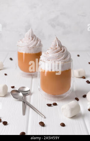 Latte macchiato di zucca con panna e spezie in bianco sullo sfondo di legno. Foto Stock