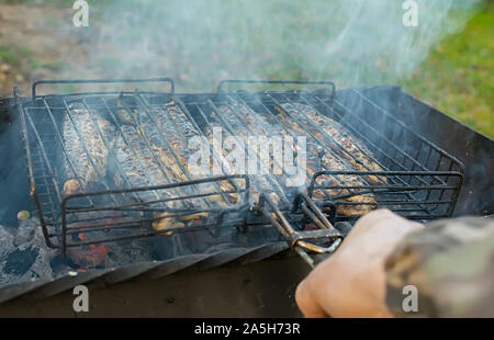 Vista la mano di un uomo con un barbecue grill con pesce fritto con limone sul chargrill all'aperto sulla natura Foto Stock