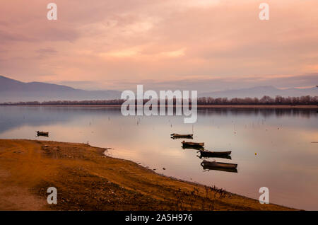 Barche in legno che galleggiano sulle acque calme del lago Kerkini al tramonto. Foto Stock