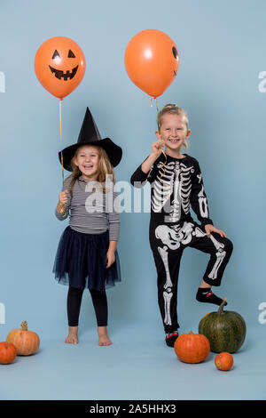 Due simpatici ragazzi di strega e lo scheletro di costumi holding arancione palloncini halloween Foto Stock