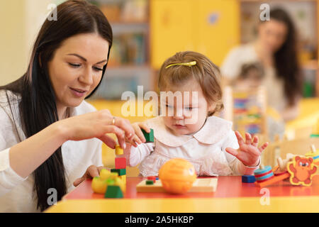 I bambini con gli insegnanti a giocare con i colori puzzle in legno in un aula montessori Foto Stock