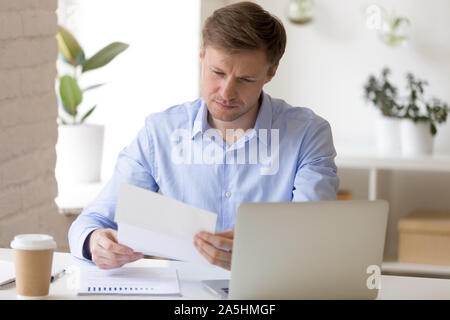 Concentrato giovane impreditore guardando attraverso il progetto di relazione di marketing. Foto Stock