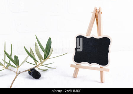 Blank outdoor chalk board stand mockup con olive branch su bianco muro di mattoni in background. Vuoto di segnaletica stradale o lavagna con cornice in legno modello Foto Stock