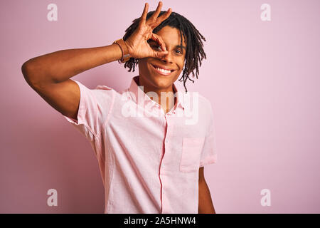 Afro-americano con dreadlocks indossando maglietta elegante in piedi isolato su sfondo rosa facendo ok gesto con la mano sorridendo, occhio guardando attraverso Foto Stock