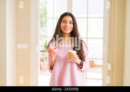 Giovane lavoratore donna prendendo una pausa mangiando una gustosa ciambella rosa e bere una tazza di caffè Foto Stock