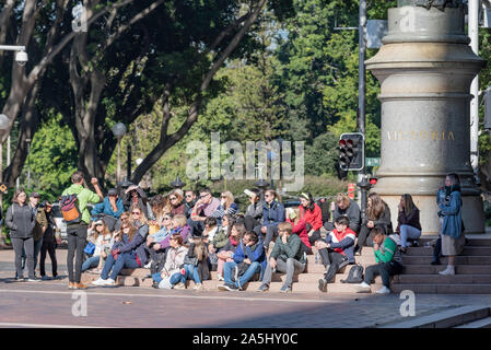 Seduta sui gradini al di sotto di una statua della regina Vittoria nel Queens Square, turisti ascoltare una guida durante un tour a piedi del quartiere affaristico di Sydney in Australia Foto Stock