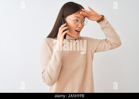 Giovane donna cinese parlando sullo smartphone isolato su sfondo bianco molto felice e sorridente guardando lontano con la mano sopra la testa. Ricerca co Foto Stock