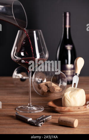 Versare il vino rosso in vetro cristallo, bottiglia, cavatappi, apriscatole, Coltello sommelier, trasparente decanter, tappi, formaggio su un tavolo di legno. Closeup, verticale Foto Stock