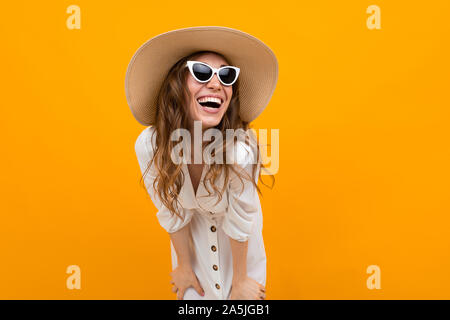 Ragazza in un cappello e occhiali contro la parete gialla ride con un largo sorriso Foto Stock