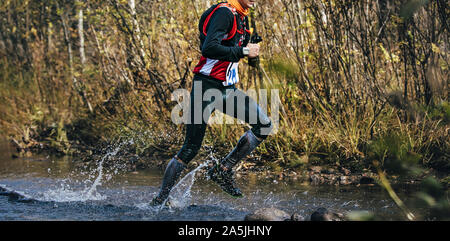 Atleta runner con camelbak esecuzione di maratona di caduta Varcando il fiume Foto Stock