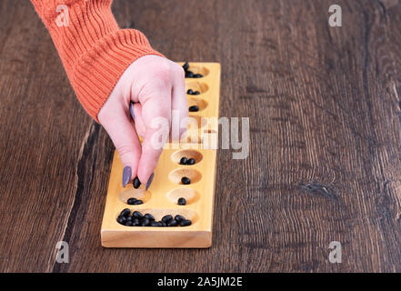 La bambina gioca un gioco di bordo mankala. La ragazza mette un chip di granella nel foro. Copia dello spazio. Giochi da tavolo concetto. Foto Stock