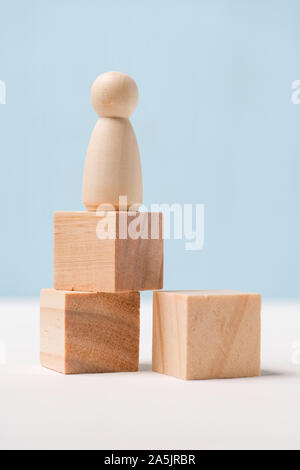 La figura di legno con i cubi su uno sfondo blu. Vincitore del concetto. Modo di successo. Close up. Verticale. Foto Stock