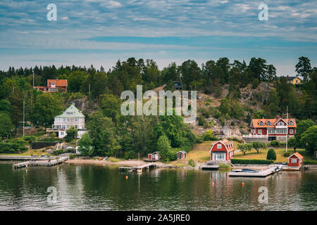 La Svezia. Molte belle rosso svedese Log in legno cabine case sull isola rocciosa costa in estate Sunny sera. Lago o fiume paesaggio. Foto Stock