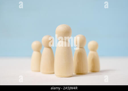 Abstract senza volto giocattolo di legno le figure dei boss nel centro e subordinati dietro di lui su sfondo blu. Foto Stock