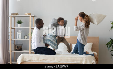 Felice famiglia multinazionale pillow fight in camera da letto Foto Stock