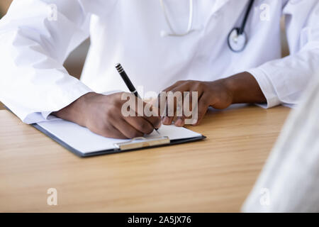 Close up biracial medico prescrizione di scrittura nella scheda medica Foto Stock