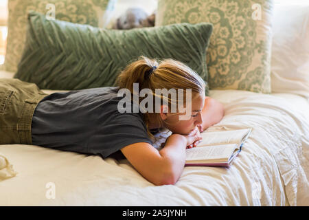 13 enne ragazza distesa nel suo letto la lettura dalla luce della finestra Foto Stock