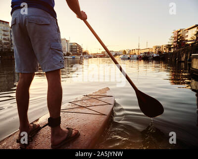 Uomo in piedi su paddleboard sul fiume all'alba, inquadratura da dietro Foto Stock