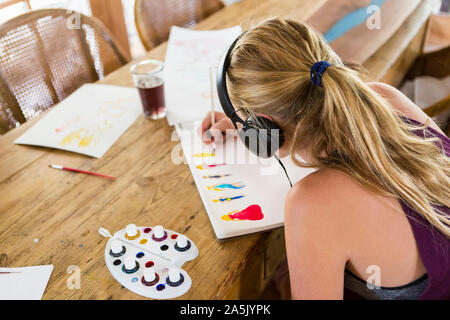 13 anno vecchia ragazza che indossa le cuffie, facendo disegno ad acquerello Foto Stock