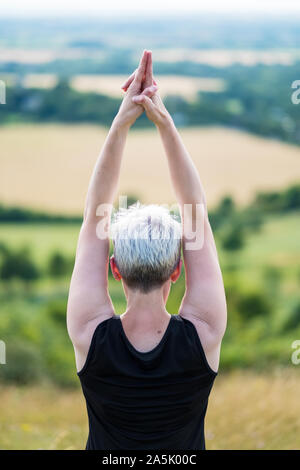 Donna matura, prendendo parte a una lezione di yoga sul pendio di una collina. Foto Stock
