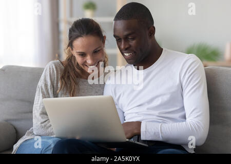 Felice coppia internazionale rilassarsi a casa utilizzando laptop Foto Stock