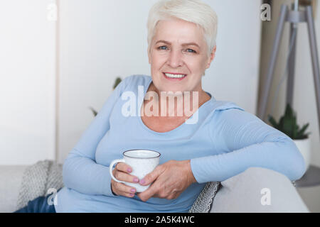 Senior bella donna seduta sul divano di casa, bere il tè Foto Stock
